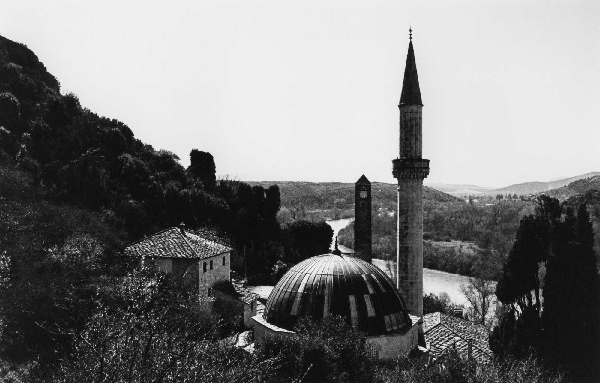 A domed mosque and minaret above a river valley, in black and white