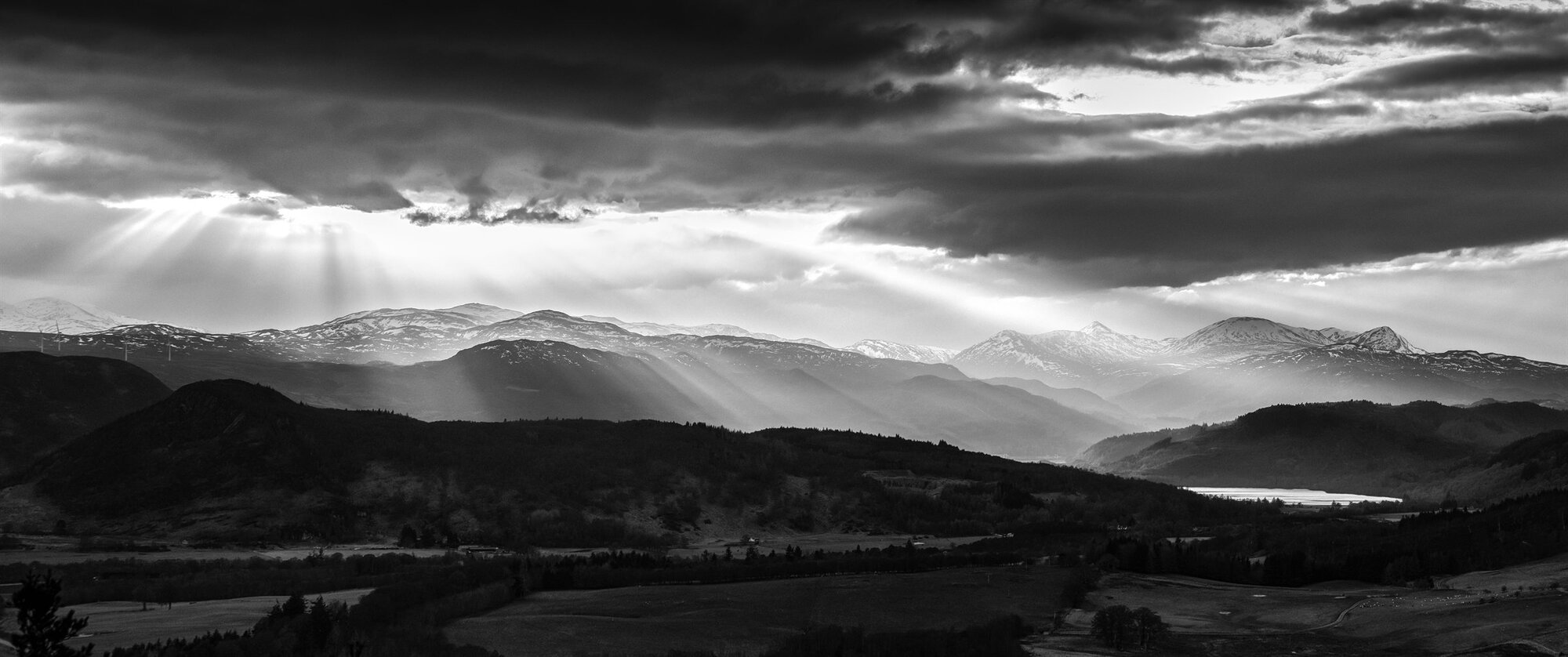 Sunbeams breaking through cloud over hills and a loch