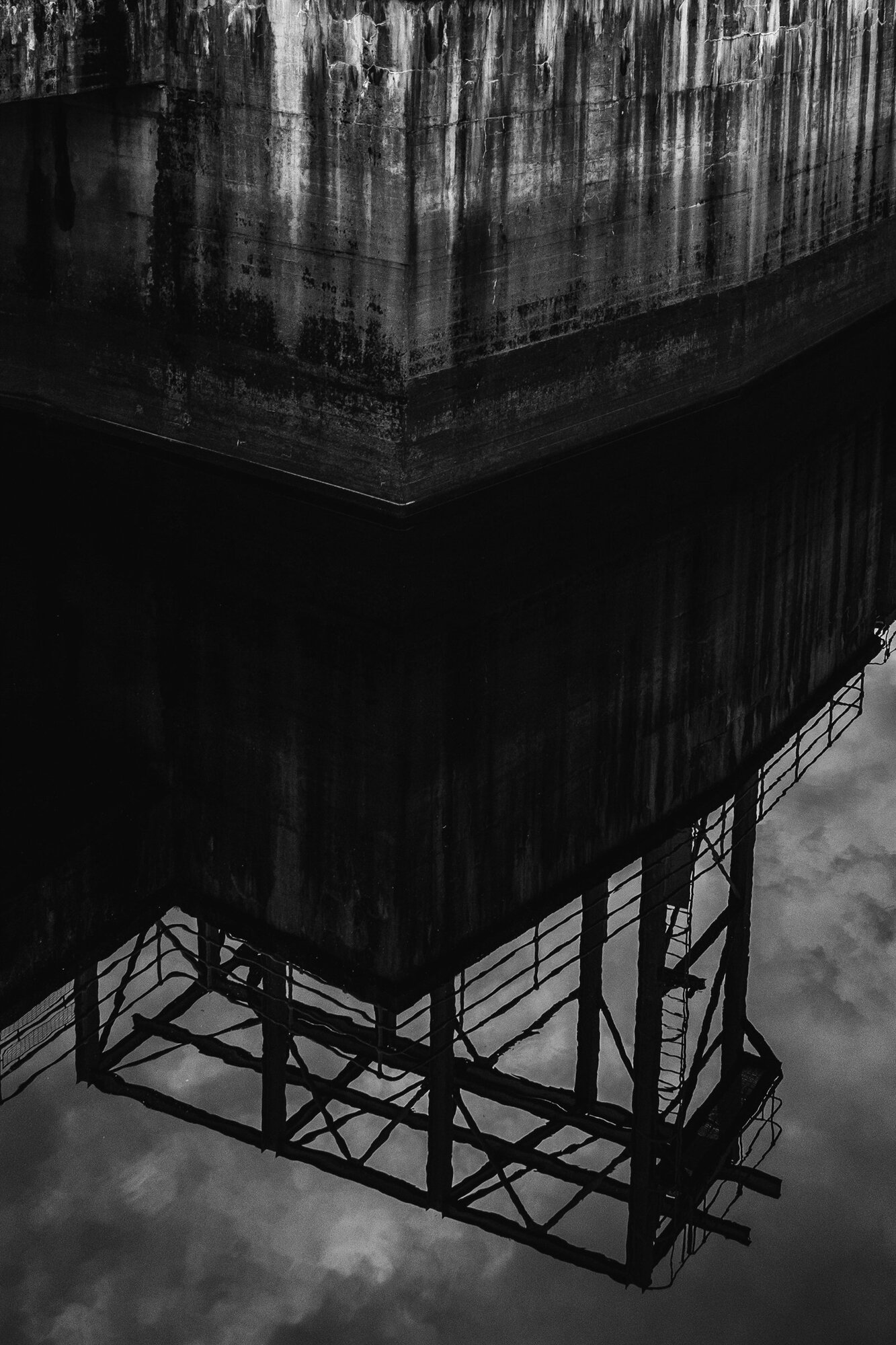 A tower and its gantry reflected upside down in dark water
