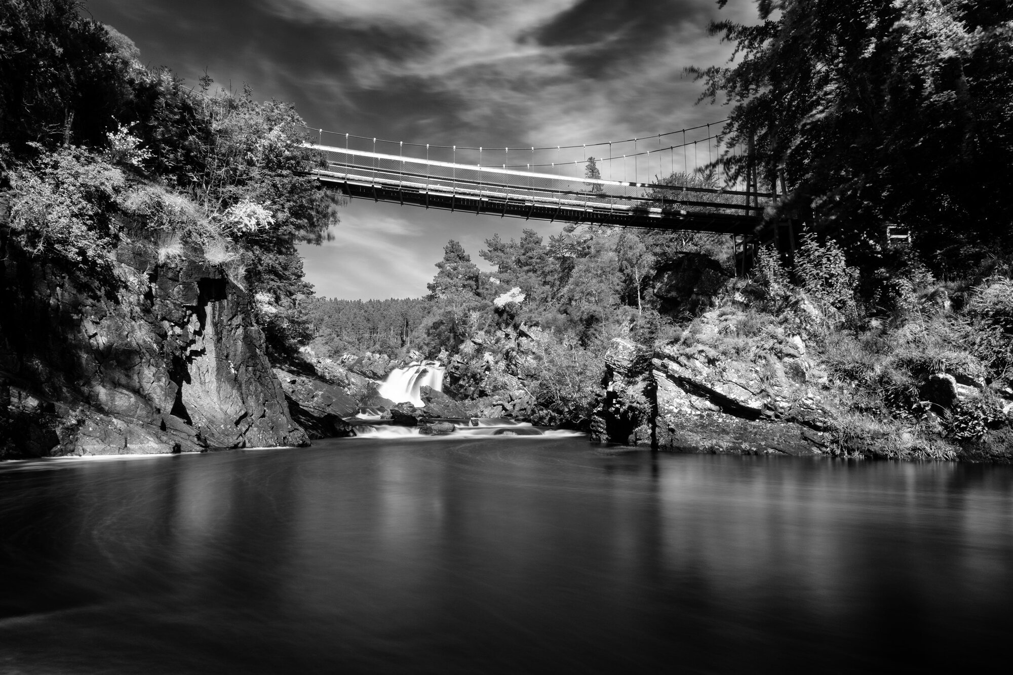 A footbridge high over a still pool in a wooded gorge