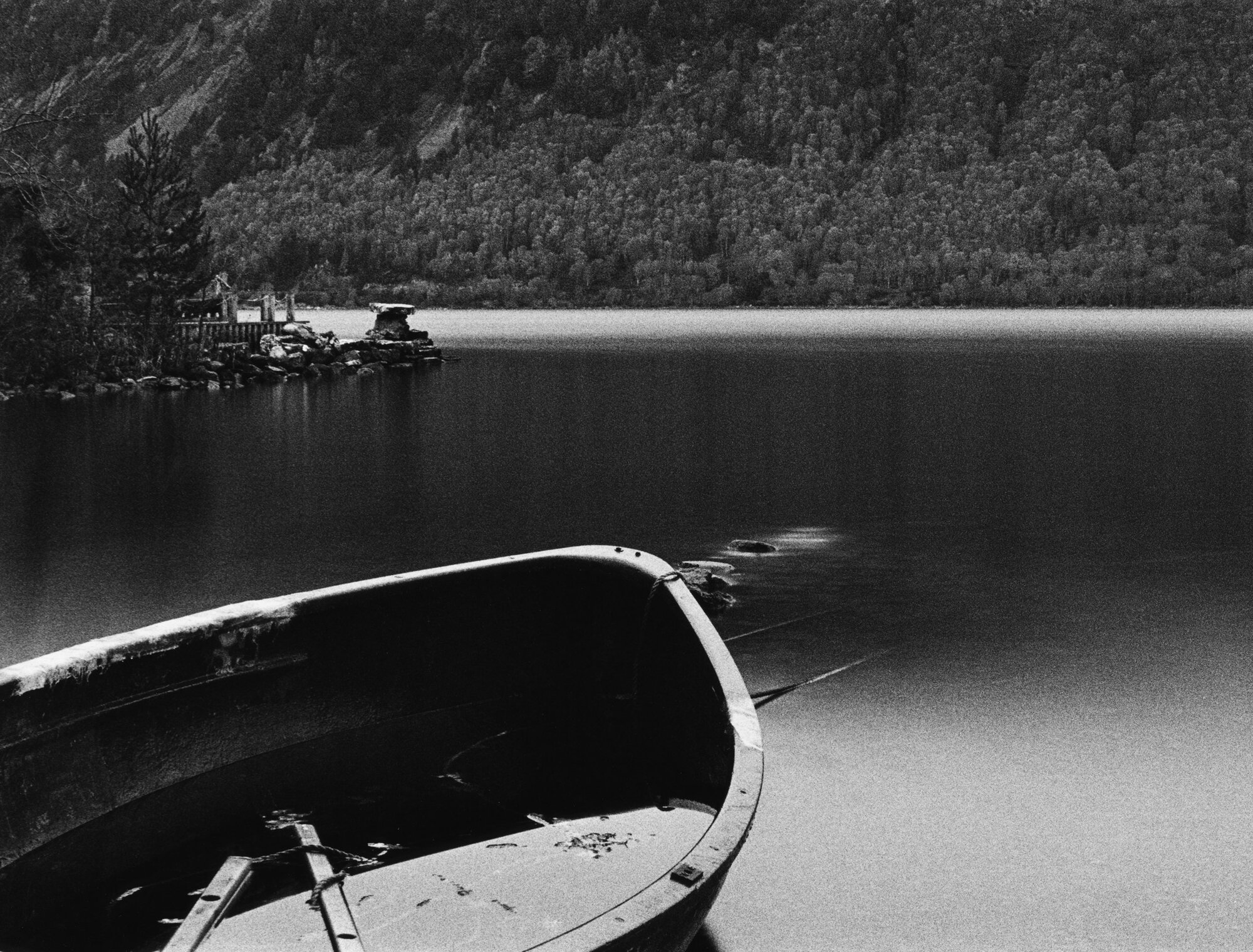 A rowing boat on a still loch beneath wooded hills