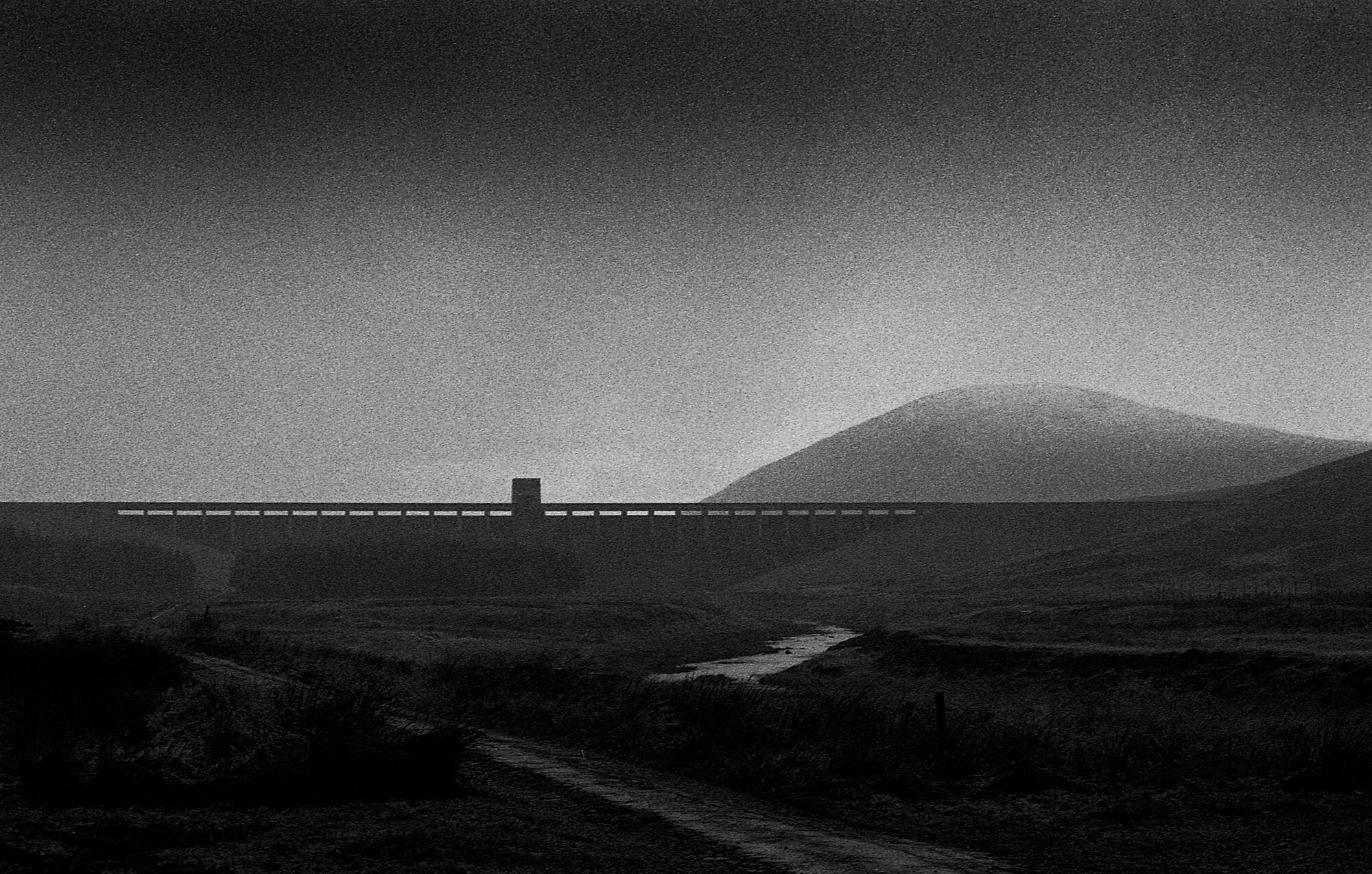 A dam wall beneath a hill in the mist