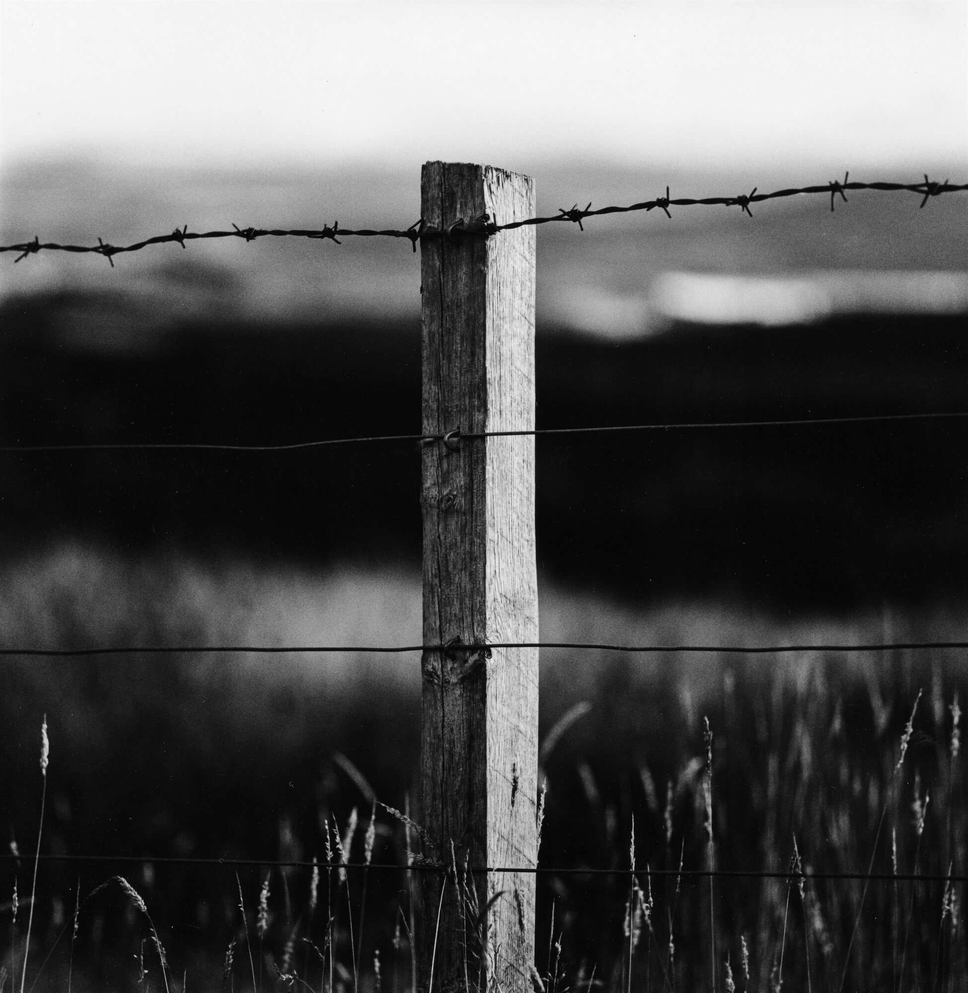 A fence post and barbed wire before dark hills