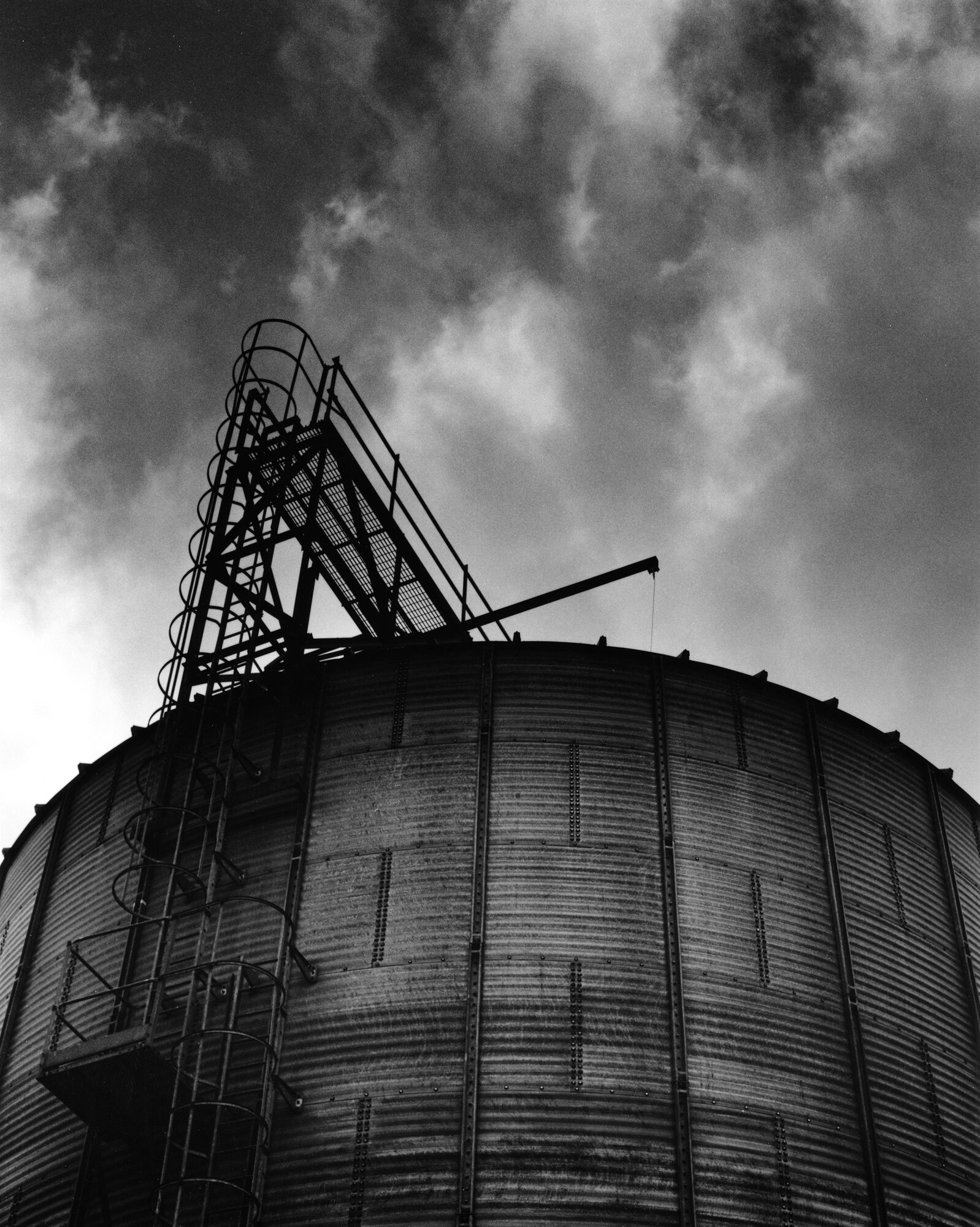 The top of a grain silo and its ladder under cloud