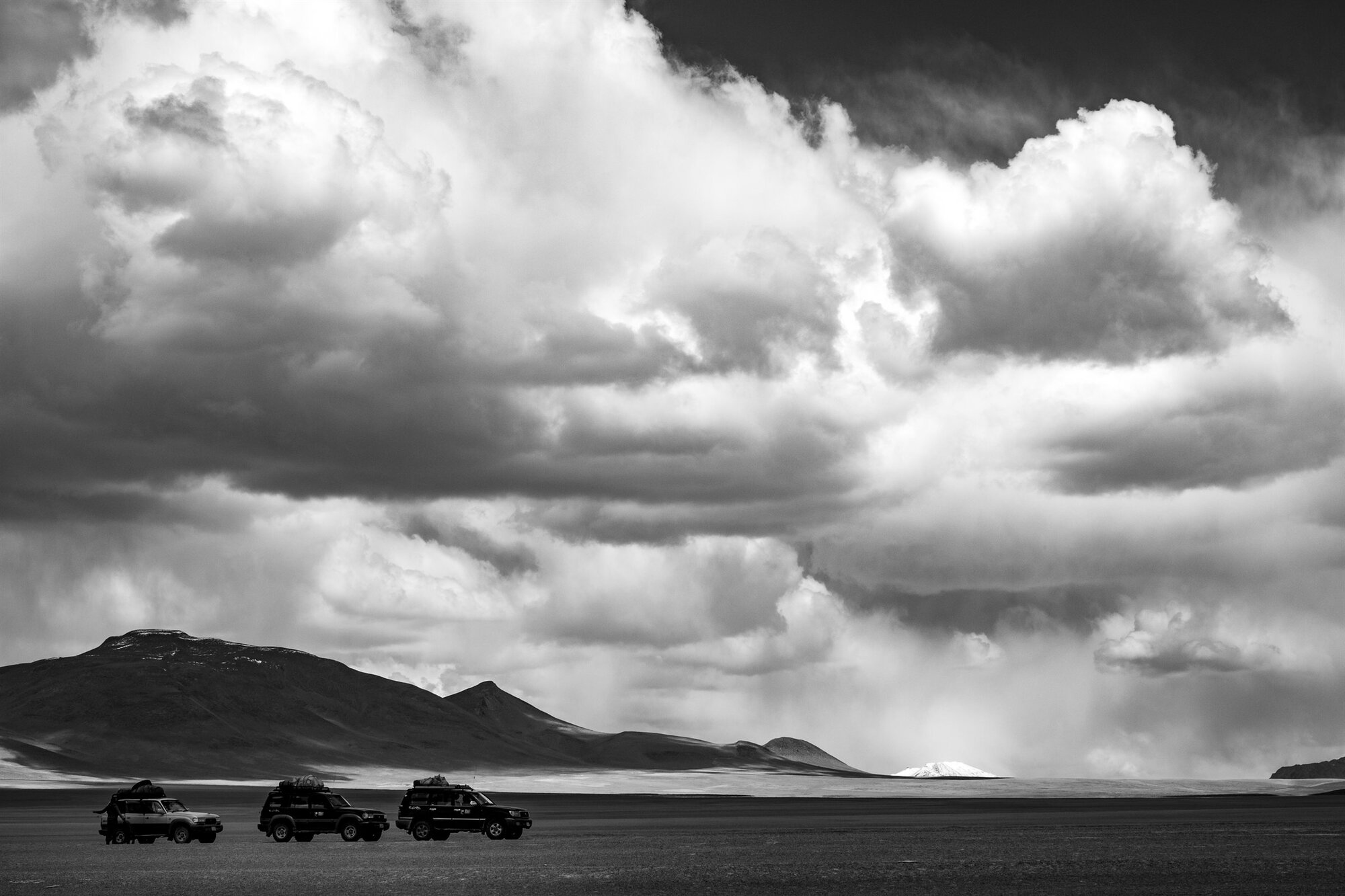 Towering storm clouds over the plain, jeeps beneath