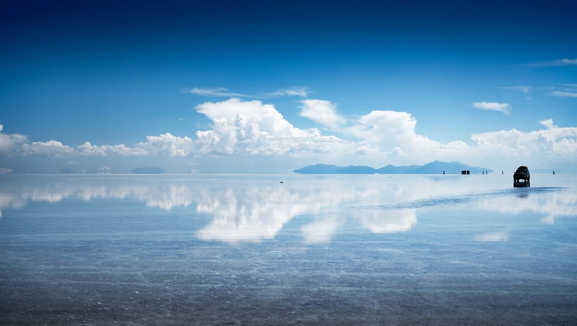 Jeeps mirrored on the wet salt flats under blue sky