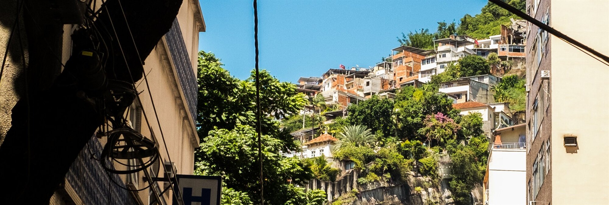 Houses climbing a green hillside under a blue sky