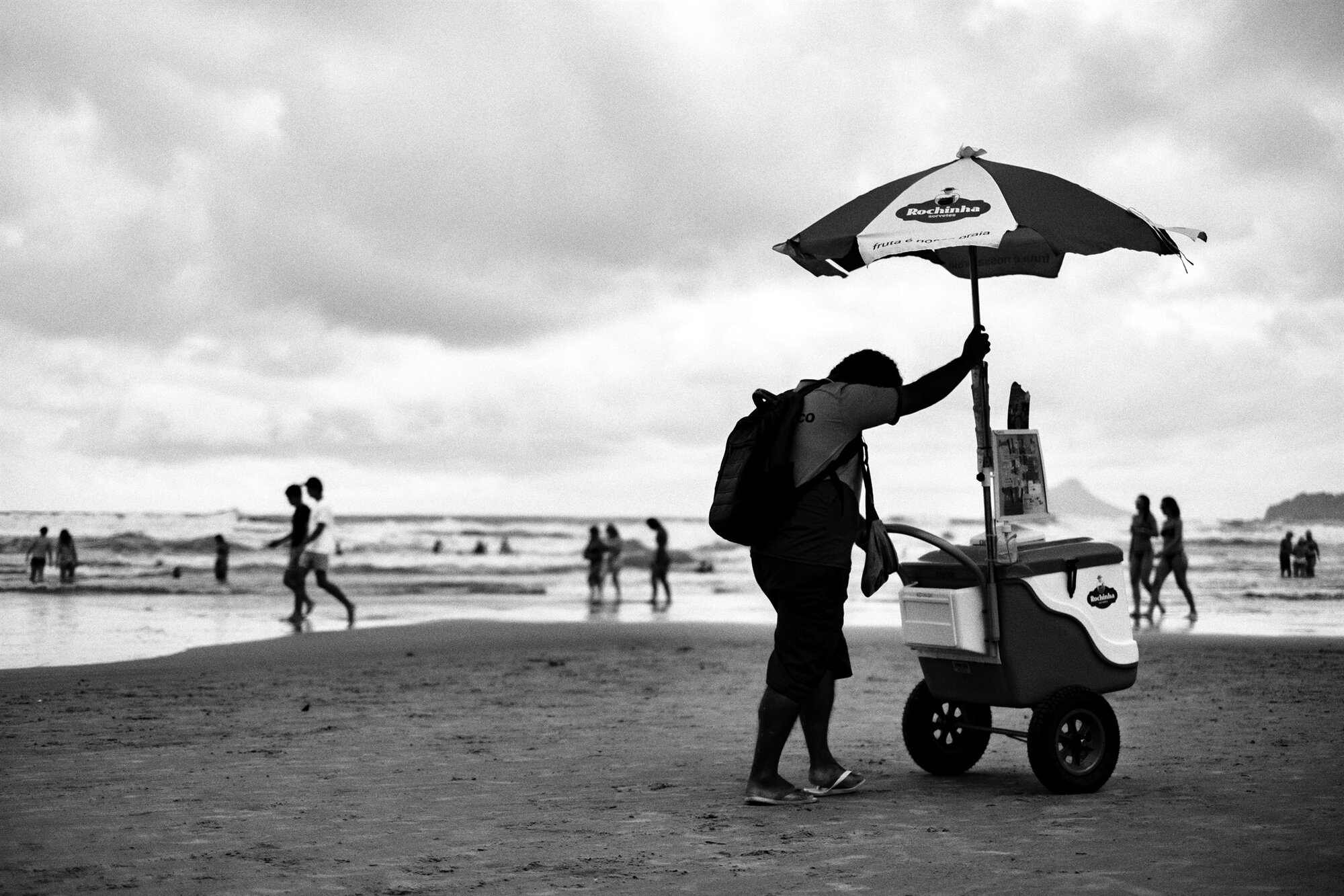 A beach vendor with an umbrella and cart