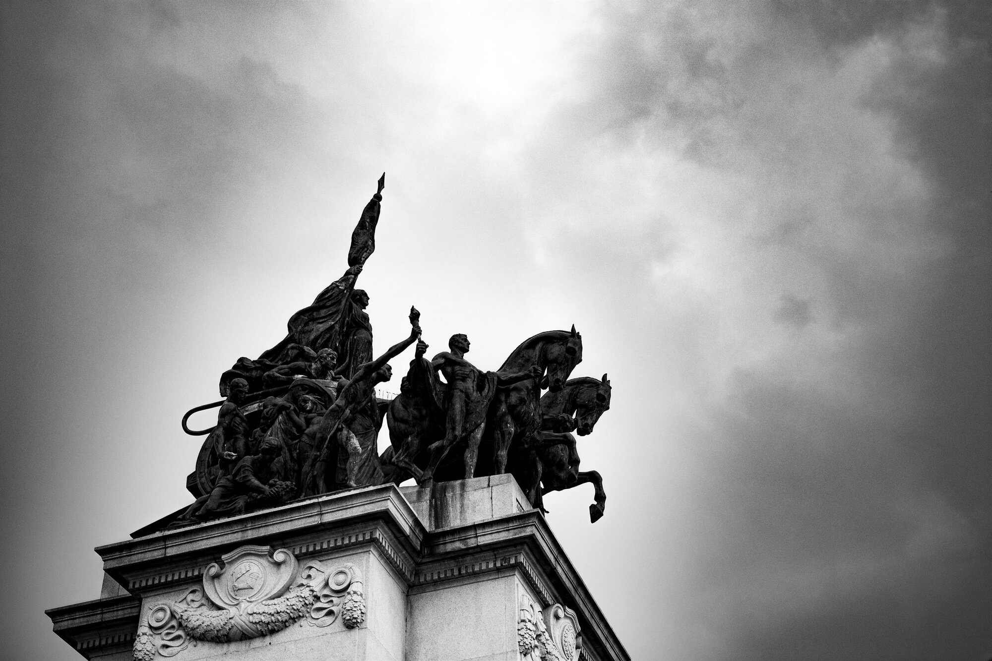A statue of horses and riders against a bright sky