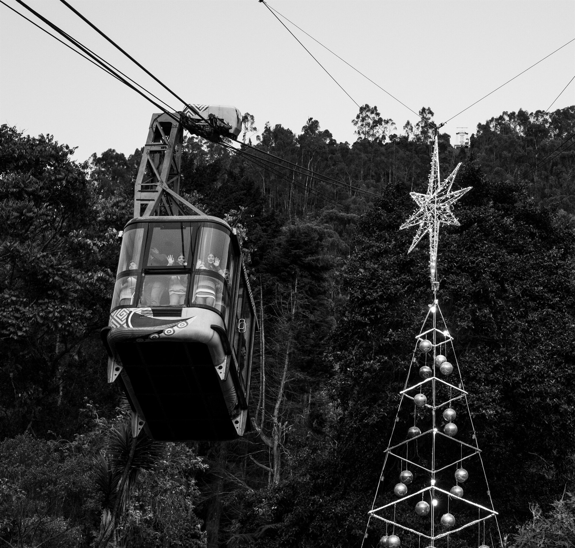 A cable car gliding past a star-topped tower above the trees