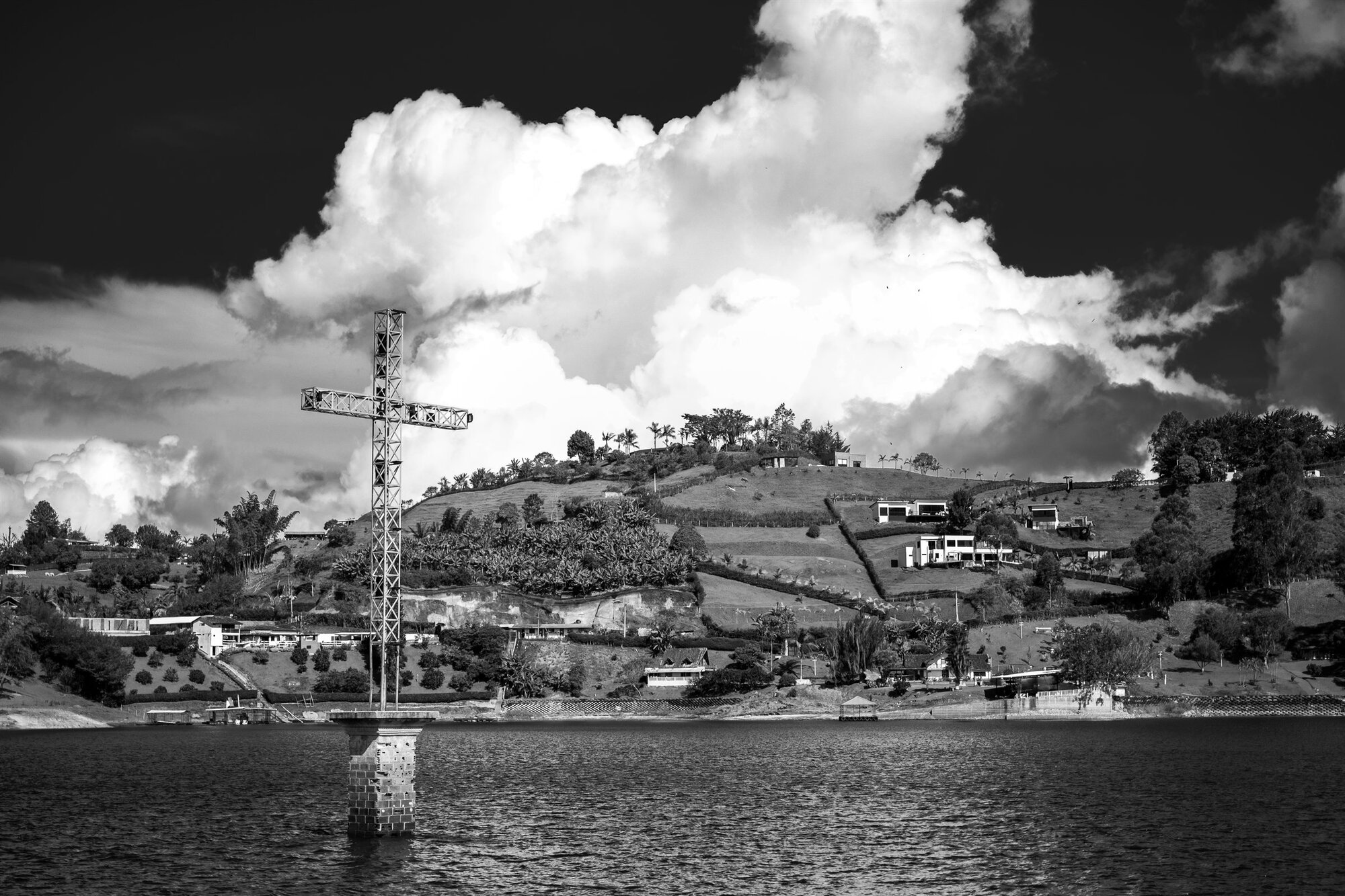 A cross on a hill above the water beneath towering cloud