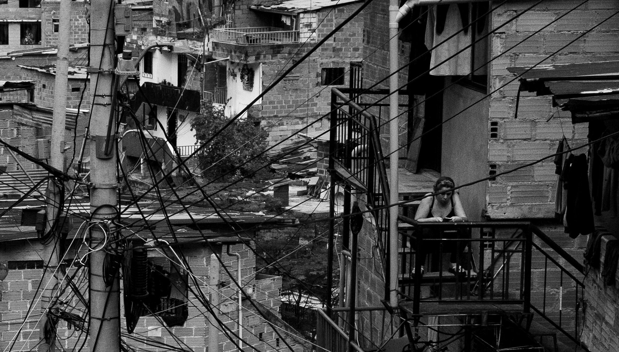 A woman on a balcony among brick houses and tangled power lines in Medellín