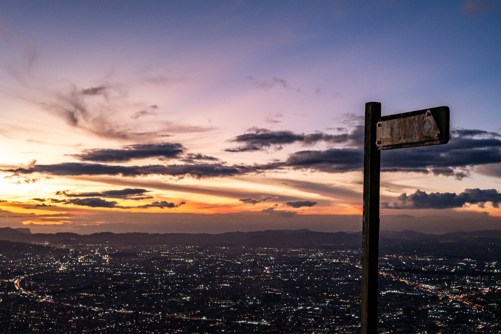 Medellín at dusk below a glowing sky, a street sign in the foreground